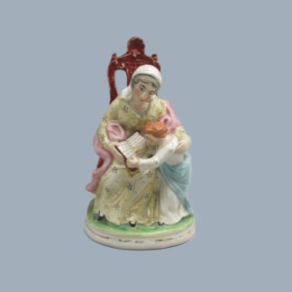 A Staffordshire figure of "The Prudent mother" she is seated with her son reading from a book.  Circa. 1870.