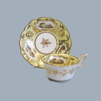 A Coalport porcelain rare yellow ground cup and saucer with three hand decorated English landscapes within shaped cartouches. Circa 1825