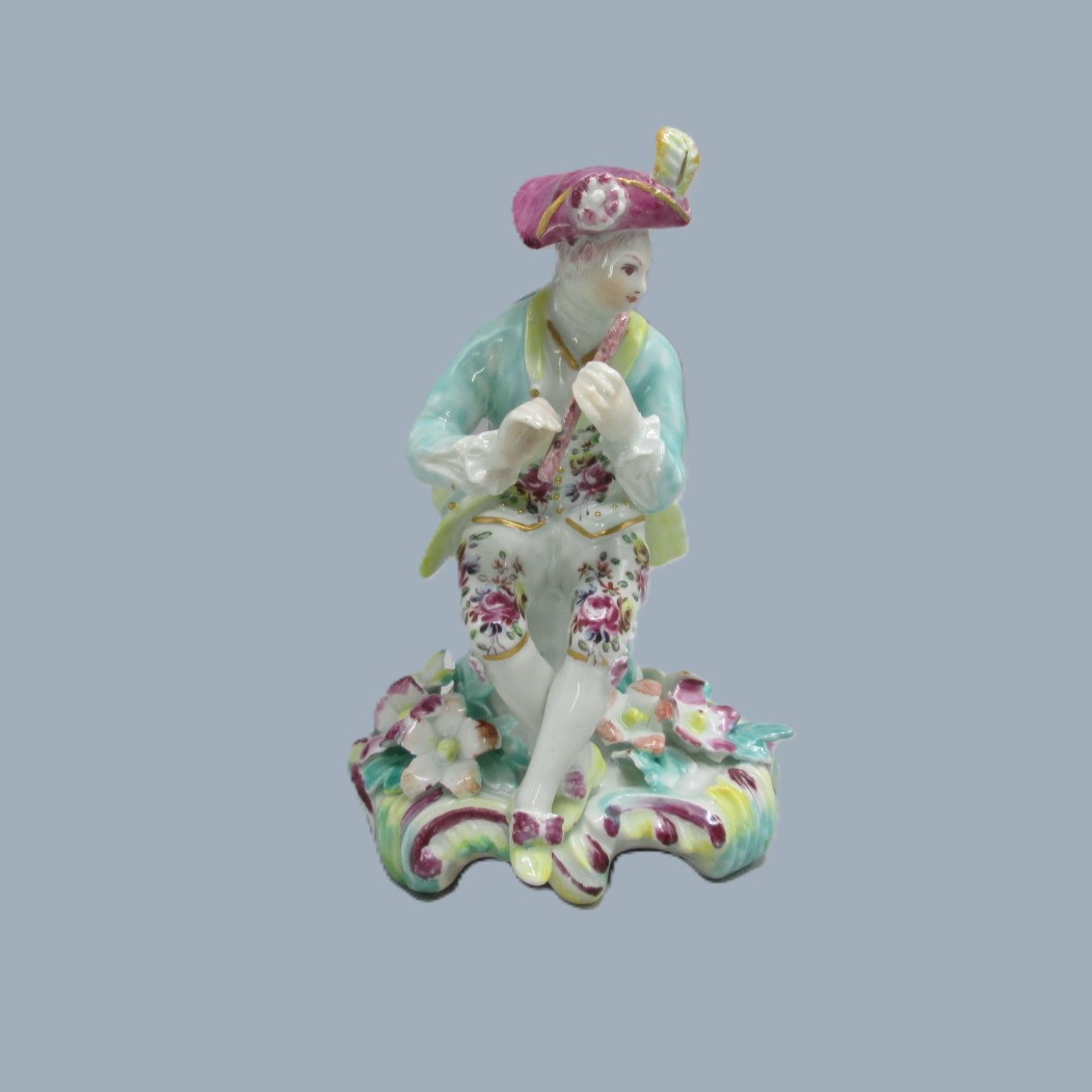 A Derby seated musician playing a flute hand decorated with a turquoise jacket and floral waistcoat and trousers. Circa 1756